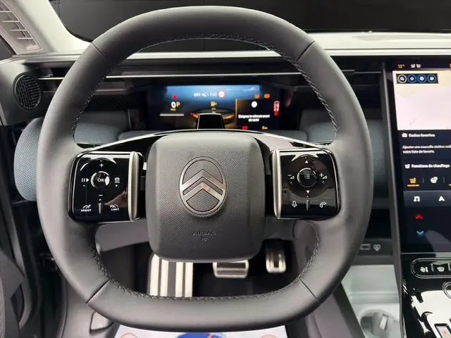 Vue rapprochée du volant noir multifonctions du Citroën C5 Aircross hybride 2026 avec tableau de bord numérique en arrière-plan.