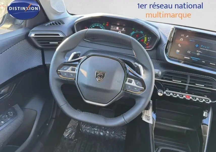 Vue intérieure centrée sur le volant cuir et le tableau de bord numérique de la Peugeot 208 gris 2025.