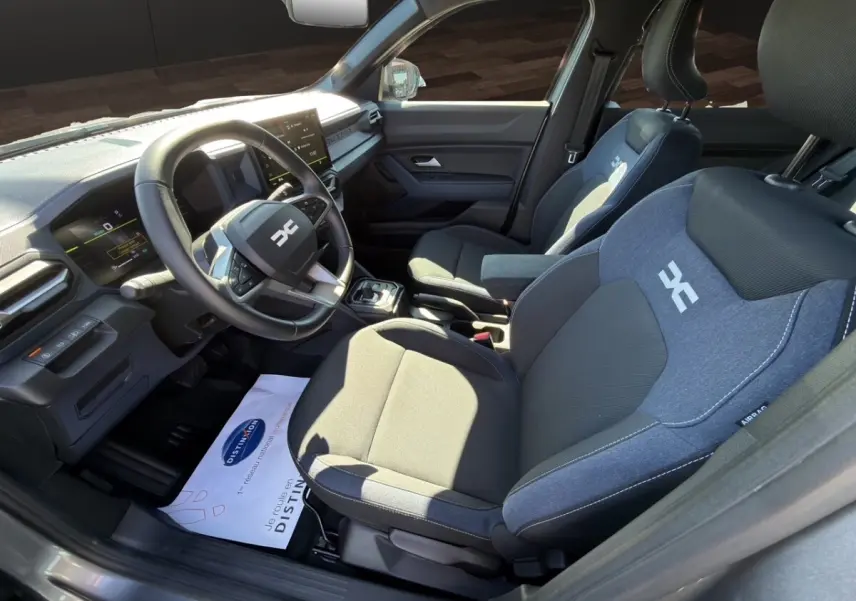 Vue intérieure côté conducteur du Dacia Duster gris foncé 2025, volant cuir multifonctions et sièges tissu bi-ton avec logo.