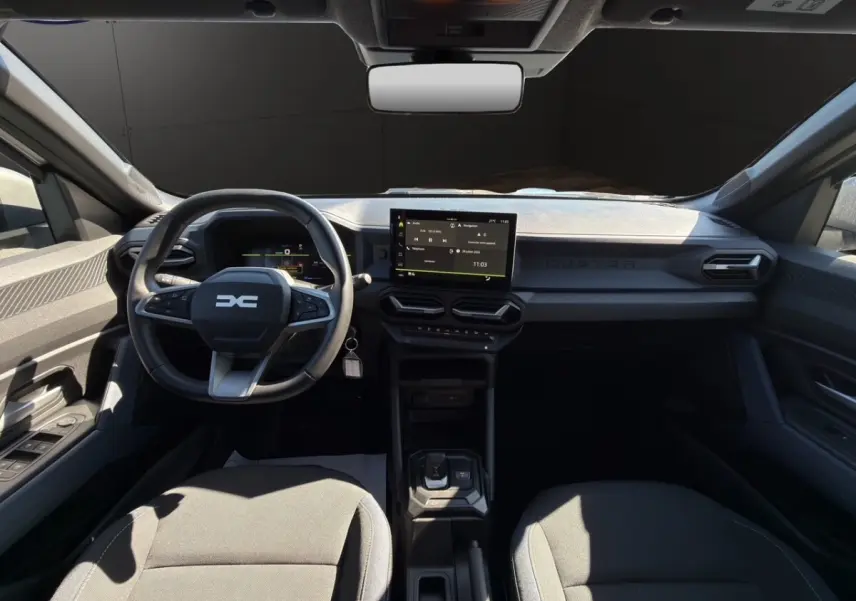 Vue intérieure avant du Dacia Duster gris foncé 2025, volant cuir multifonctions et écran tactile central visible.