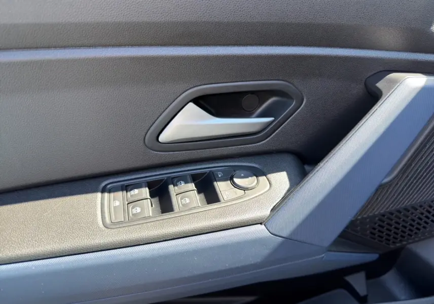 Gros plan sur la porte côté conducteur du Dacia Duster gris foncé, montrant les commandes des vitres et la poignée intérieure.