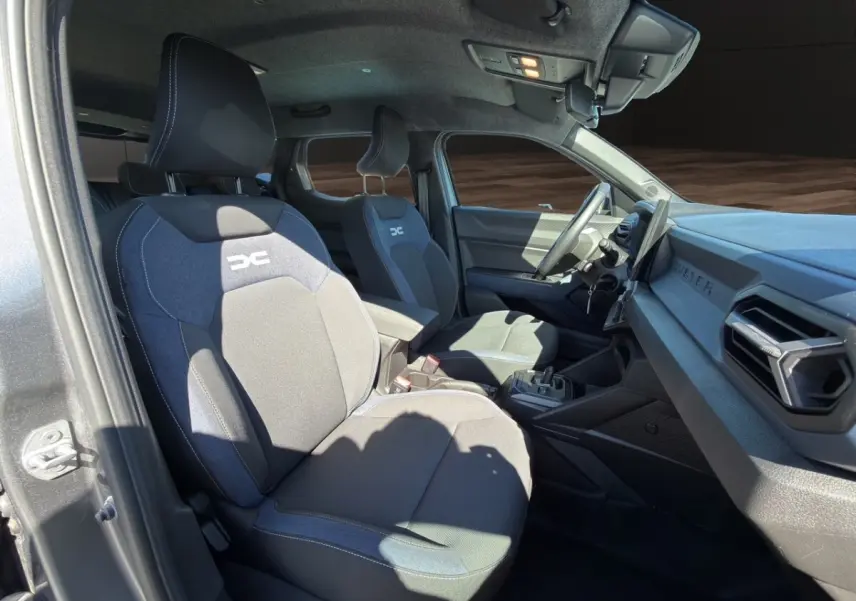 Vue intérieure côté conducteur du Dacia Duster gris foncé 2025, sièges tissu avec logo DC et tableau de bord moderne.