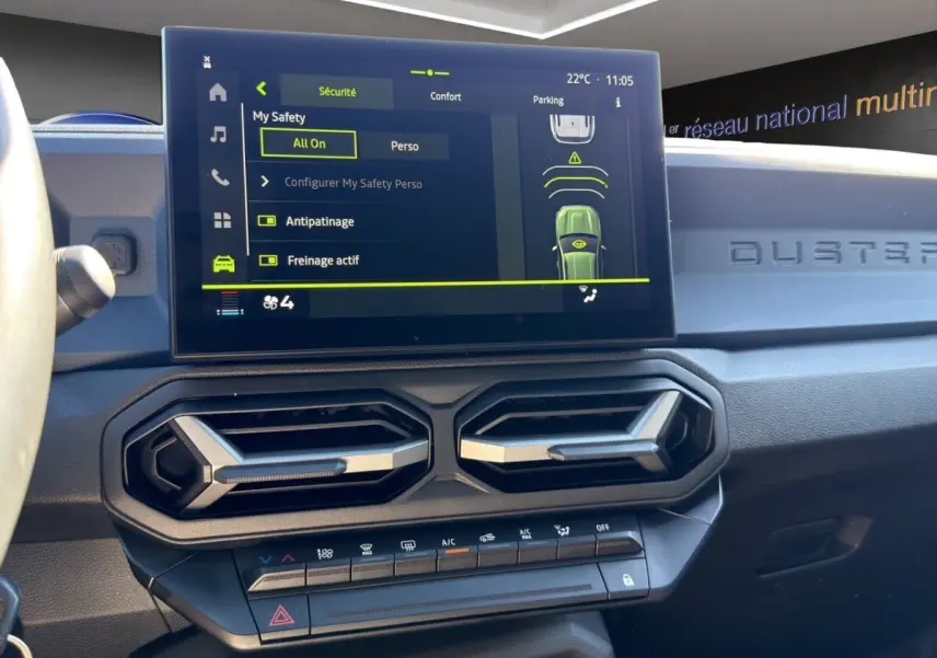 Vue intérieure du tableau de bord du Dacia Duster gris foncé, avec écran tactile central affichant les aides à la conduite.