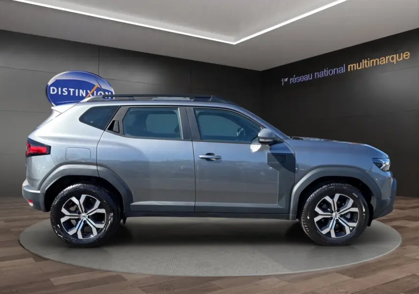 Vue de profil côté gauche d'un Dacia Duster gris foncé 2025 avec rails de toit noirs et jantes alliage.