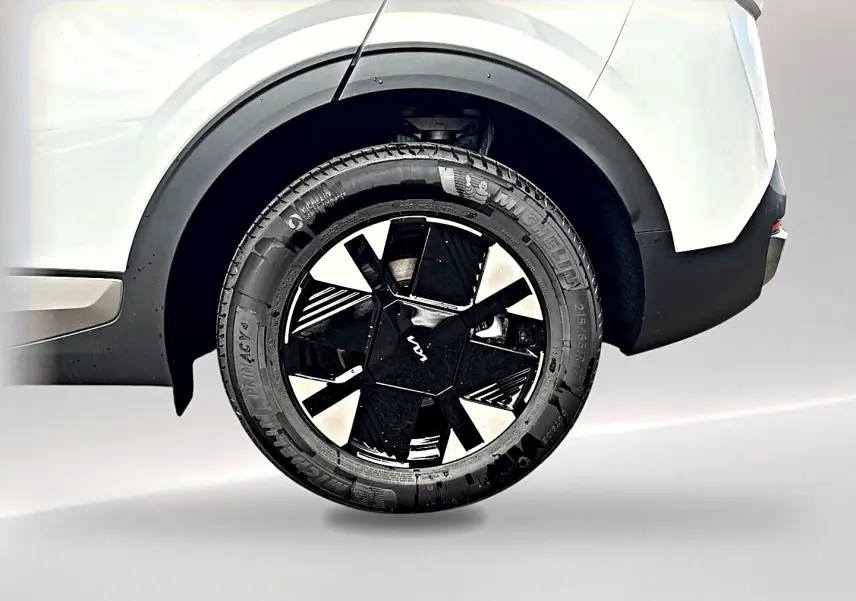 Gros plan sur la roue arrière droite noire et blanche du KIA SPORTAGE 1.6 hybride blanc, avec jante alu au design moderne.