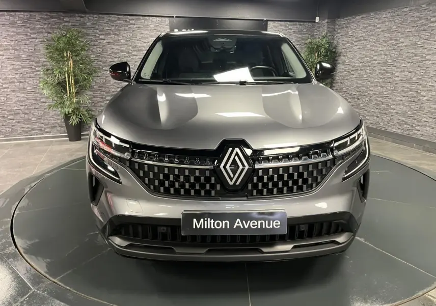 Vue avant d'un Renault Austral gris avec calandre à damier chrome sombre et toit noir étoilé en intérieur showroom.