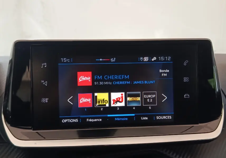 Écran tactile central de 7 pouces du Peugeot 208 blanc, affichant la radio FM avec stations et température extérieure.