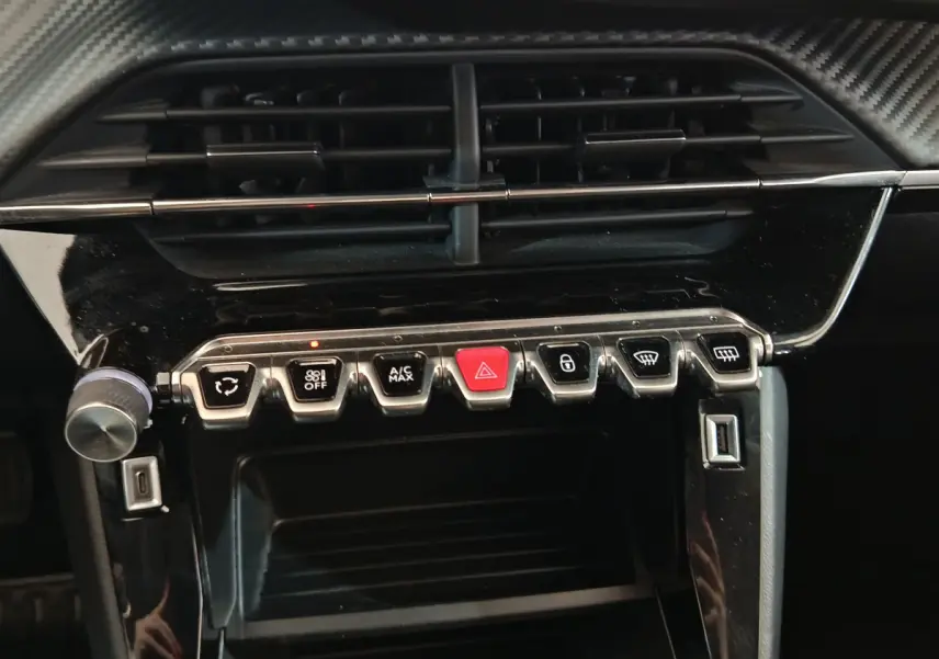 Gros plan sur la console centrale de la Peugeot 208 blanche, montrant les commandes de climatisation et les boutons fonctionnels.