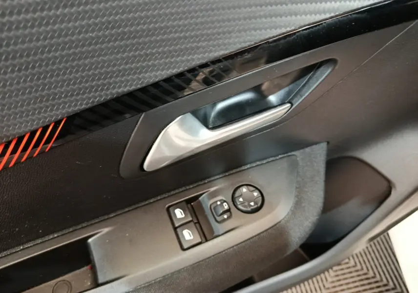 Gros plan sur la porte côté conducteur de la Peugeot 208 blanche, avec commandes électriques et poignée argentée.