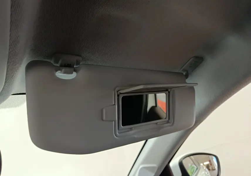 Miroir de courtoisie ouvert sur le pare-soleil côté conducteur dans l'habitacle clair d'une Peugeot 208 blanche.