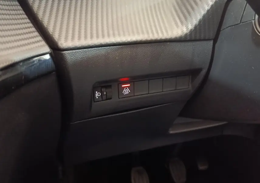 Détail du tableau de bord côté gauche d'une Peugeot 208 blanche, avec bouton d'assistance désactivée allumé en rouge.