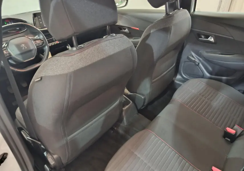 Vue intérieure arrière de la Peugeot 208 blanche, sièges tissu noir avec surpiqûres rouges et tableau de bord visible au loin