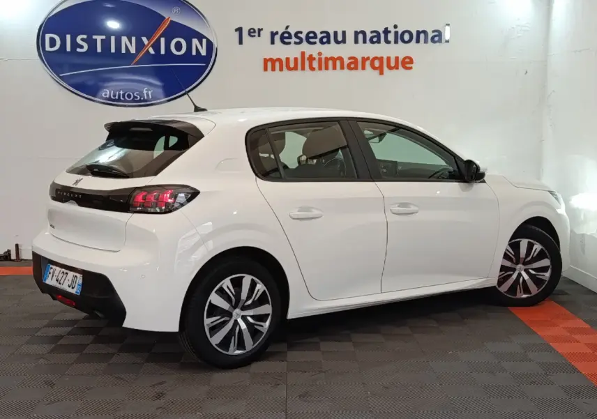 Peugeot 208 blanc vue de profil côté droit, stationnée en intérieur avec feux arrière LED allumés.