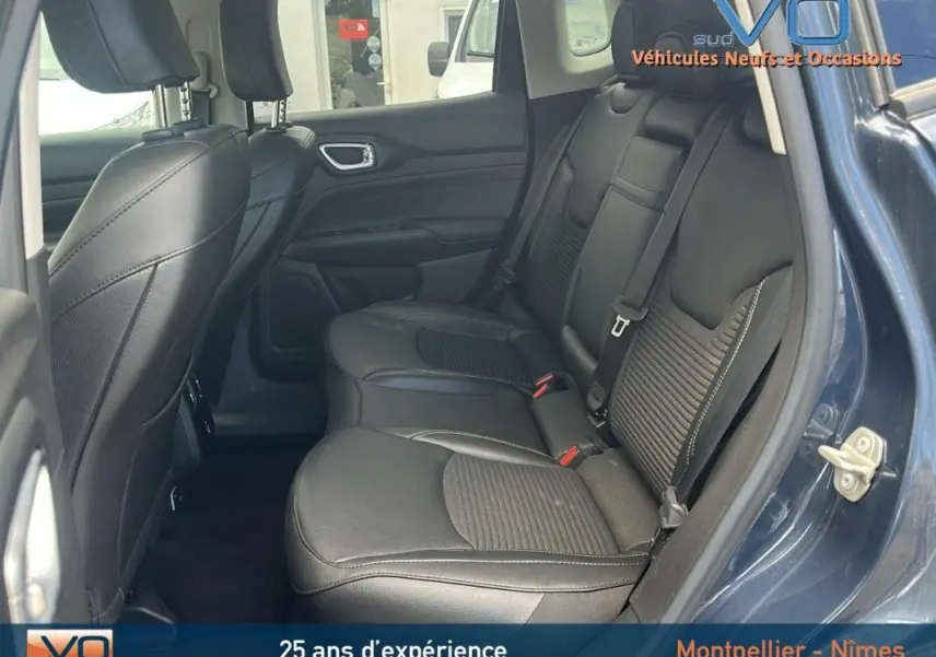 Vue intérieure arrière du Jeep Compass bleu 2023, sièges en cuir noir avec accoudoir central et ceintures visibles.