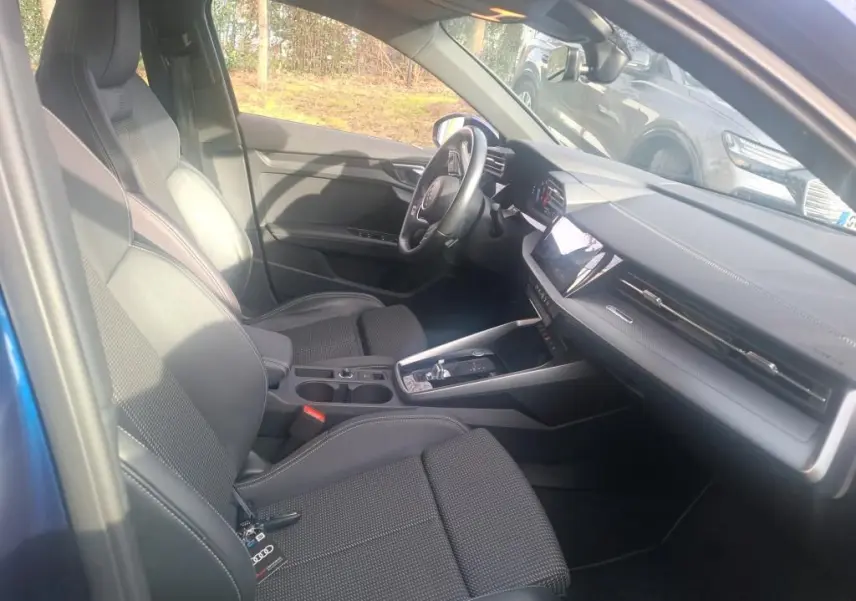 Vue intérieure côté conducteur de l'Audi A3 2.0 TDI 150 S-Tronic S-Line 2022 avec sièges tissu noirs et tableau de bord moderne.