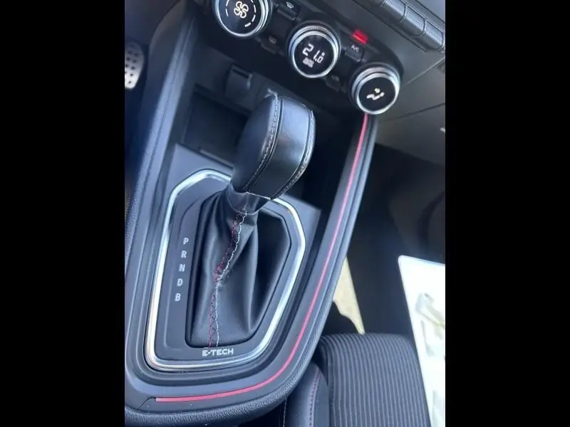 Gros plan sur la console centrale de la Renault Clio V gris métal, avec levier de vitesse automatique et surpiqûres rouges.