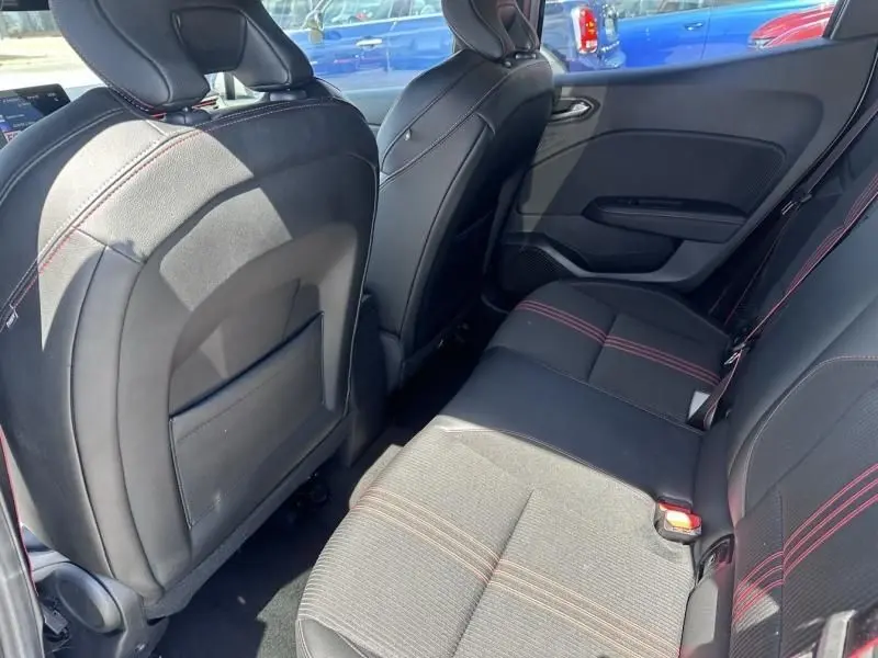 Vue intérieure arrière côté droit de la Renault Clio V gris métal, sièges noirs avec surpiqûres rouges distinctives.