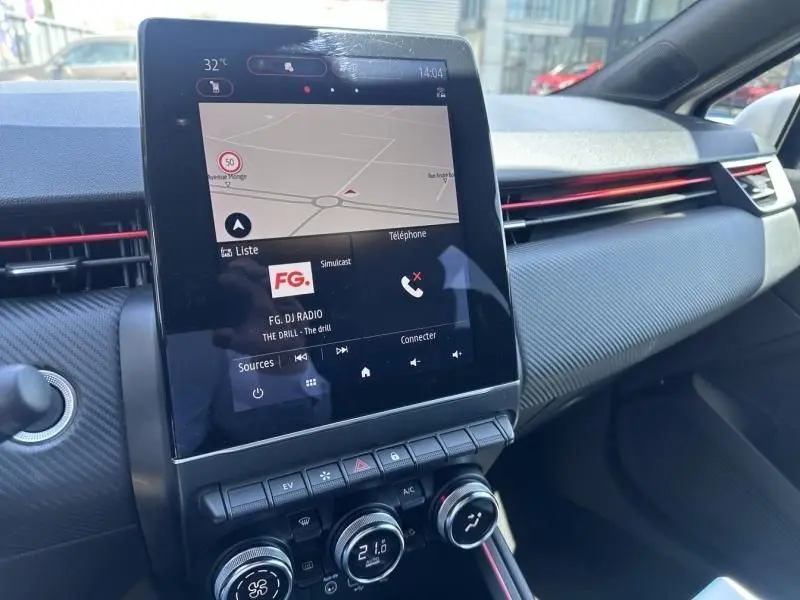 Vue intérieure centrée sur l'écran tactile et la console de la Renault Clio V gris métal, version RS Line avec détails rouges.