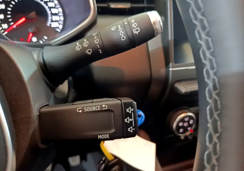 Gros plan sur la commande multifonction noire à gauche du volant cuir d'une Renault Clio Business blanche, tableau de bord en arrière-plan.