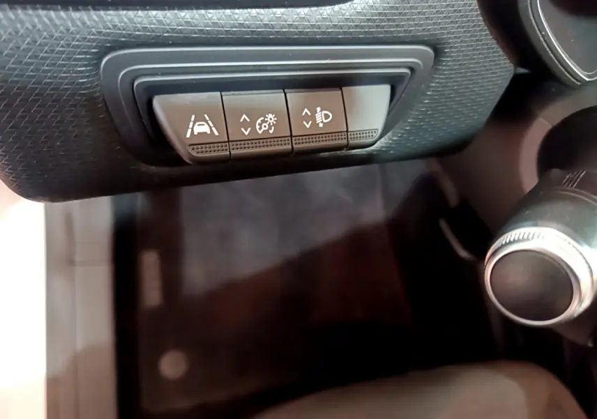 Gros plan sur les commandes d'assistance à la conduite sous le tableau de bord d'une Renault Clio Business blanche.