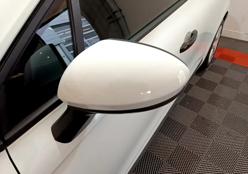 Rétroviseur blanc côté gauche de la Renault Clio Business 2021, avec poignée de porte visible sur fond de sol texturé.