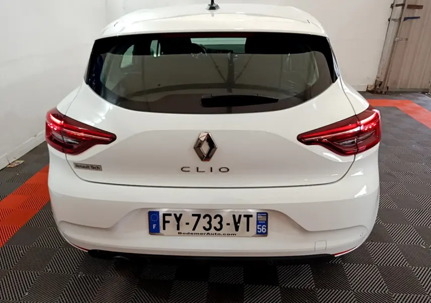 Vue arrière d'une Renault Clio blanche 2021 avec feux LED et logo Renault centré sur un sol à damier noir et orange.