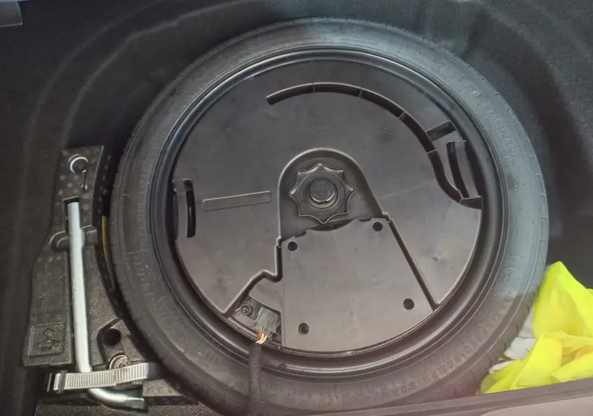 Gros plan sur la roue galette de secours dans le coffre d'une Volkswagen Golf bleue 2022, avec outil de levage visible.