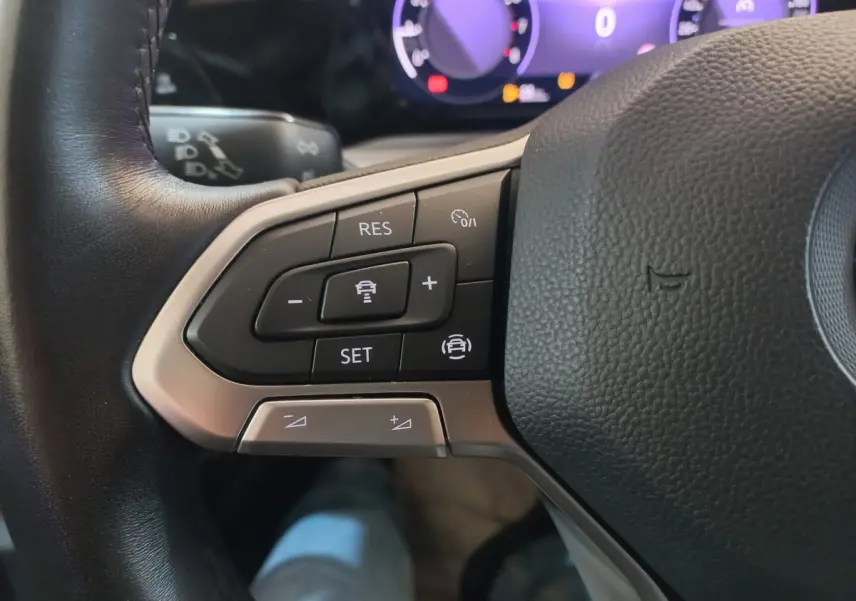 Gros plan sur les commandes du volant côté gauche de la Volkswagen Golf 1.5 bleu, avec tableau de bord numérique en arrière-plan.