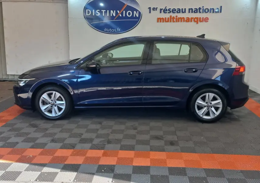 Profil côté gauche d'une Volkswagen Golf bleu 2022 garée en intérieur sur sol à damier gris et orange.