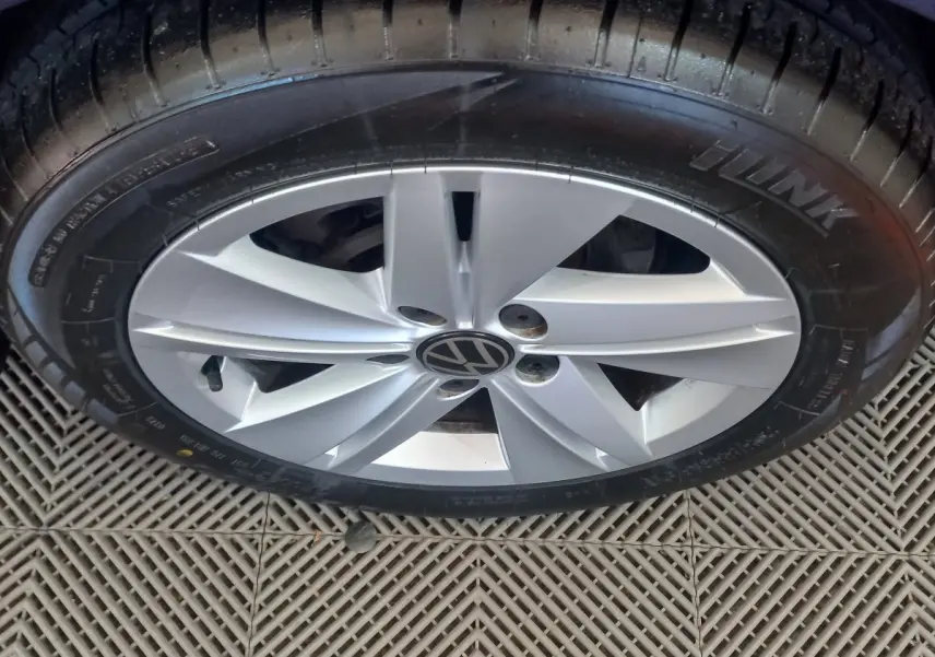 Gros plan sur la jante argentée avec logo Volkswagen d'une Golf bleue, vue du dessus sur sol carrelé.