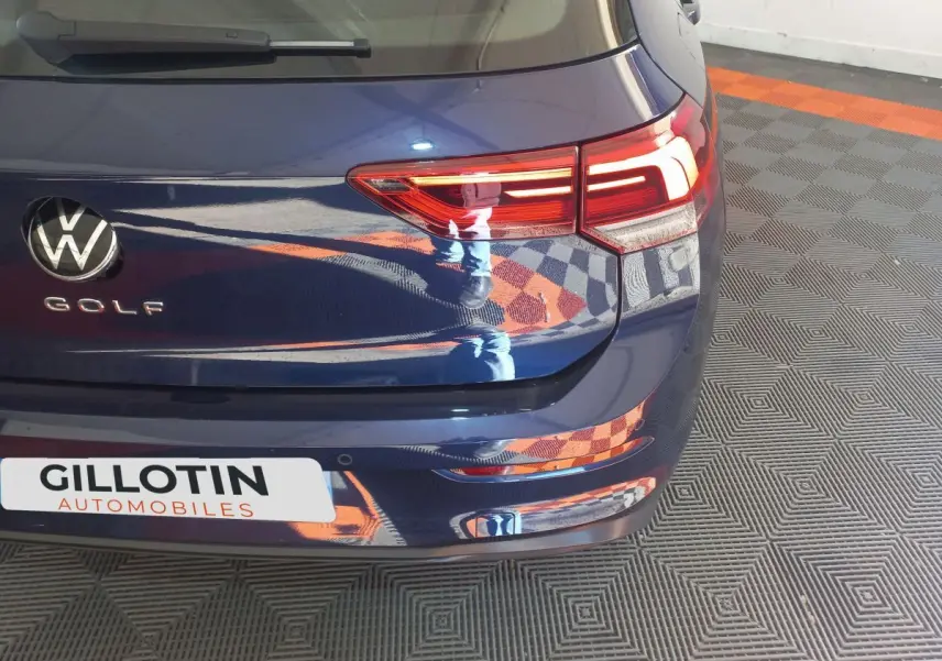 Vue arrière droite d'une Volkswagen Golf bleue avec feux LED et logo VW visible sur un sol à damiers.