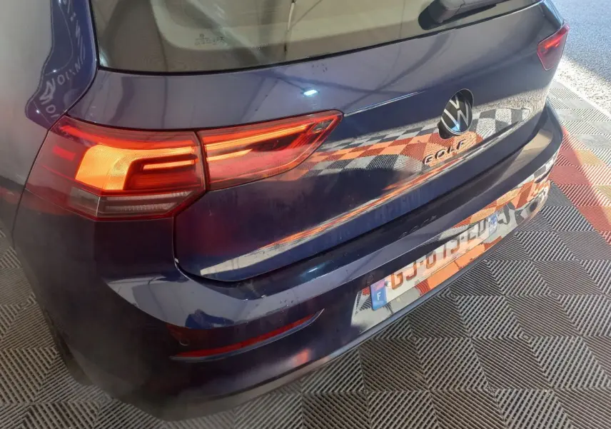 Vue 3/4 arrière droite d'une Volkswagen Golf bleue 2022 avec feux arrière allumés et logo visible sur le coffre