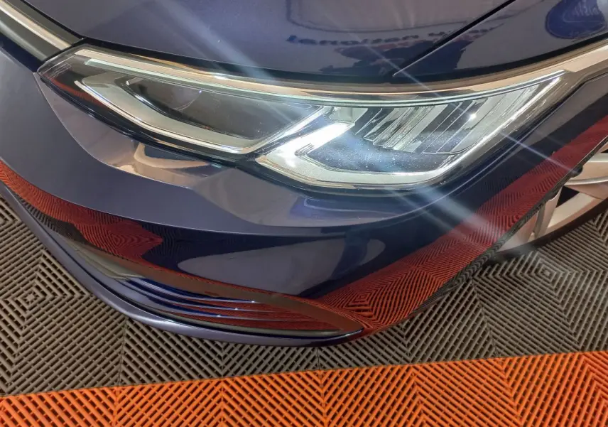 Gros plan sur le phare avant droit d'une Volkswagen Golf bleu profond avec reflets sur la carrosserie