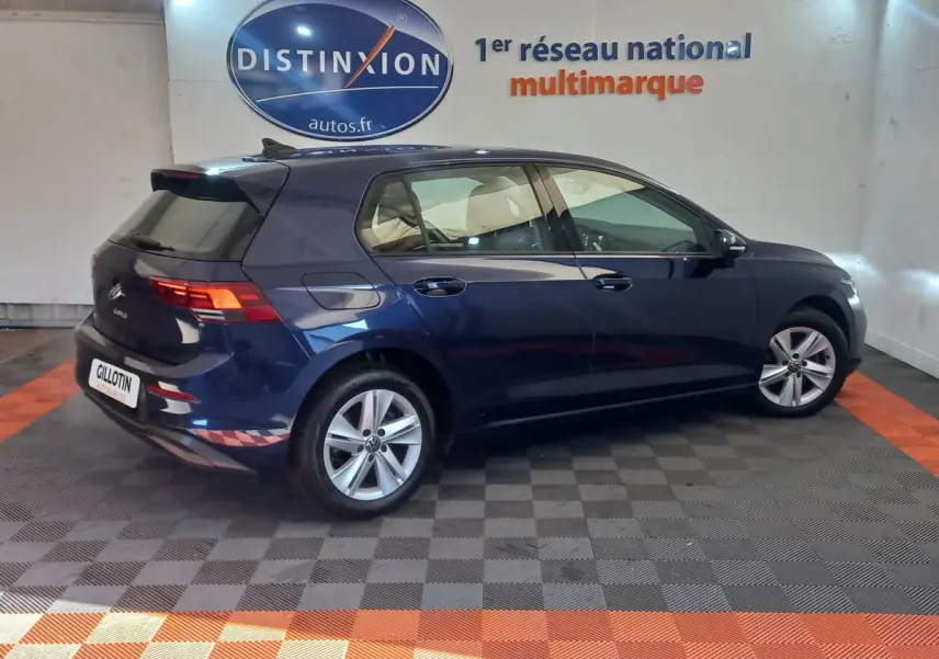 Volkswagen Golf bleu vue de profil côté droit en intérieur, avec jantes alliage et feux arrière LED allumés.