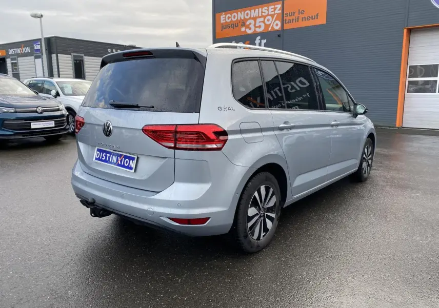 Vue 3/4 arrière droite d’un Volkswagen Touran 2025 gris argent métallisé avec attelage et vitres surteintées.