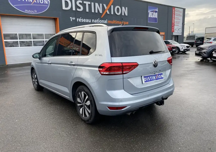 Volkswagen Touran 2025 gris Oyster, vue 3/4 arrière droit avec attelage escamotable et vitres arrière surteintées.