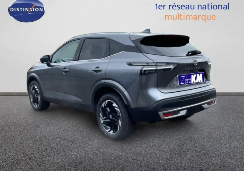 Vue 3/4 arrière droite d'un Nissan Qashqai gris 2025 avec jantes aluminium et barres de toit visibles.