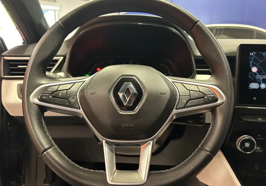 Volant en cuir avec commandes intégrées et logo Renault au centre, intérieur moderne de la Clio V gris 2023.