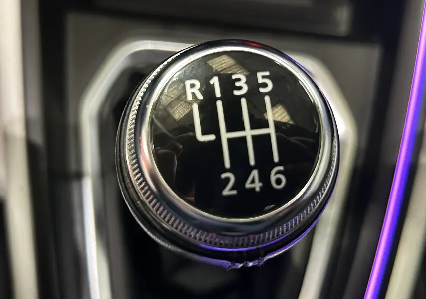 Gros plan sur le pommeau de la boîte manuelle de la Renault Clio V TCe 90 gris, avec marquage des vitesses en blanc.