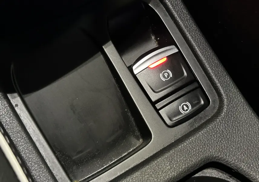 Gros plan sur le bouton de frein à main électronique rouge dans la console centrale de la Renault Clio V gris 2023.