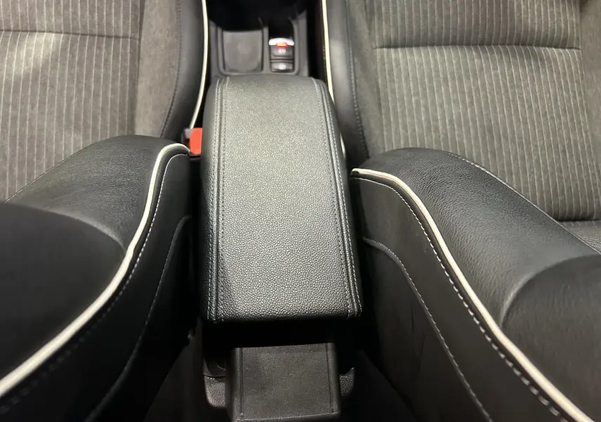 Gros plan sur l'accoudoir central noir avec surpiqûres blanches entre les sièges avant en tissu gris de la Renault Clio V.