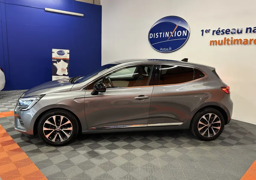 Profil côté gauche d'une Renault Clio V gris métallisé 2023, avec jantes alliage et vitres teintées en showroom.