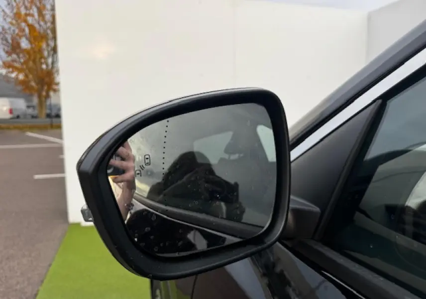 Rétroviseur extérieur côté gauche du Renault Espace VI noir étoilé, avec surface légèrement humide et reflet flou.