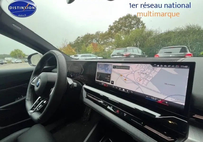 Vue intérieure côté conducteur de la BMW Série 5 gris, avec tableau de bord numérique et écran tactile large affichant la navigation.
