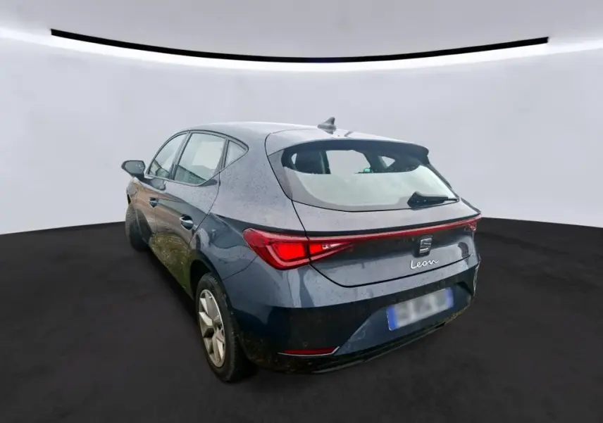 Vue 3/4 arrière droite d'une SEAT Leon gris métallisé 5 portes avec feux arrière reliés par une bande lumineuse rouge.