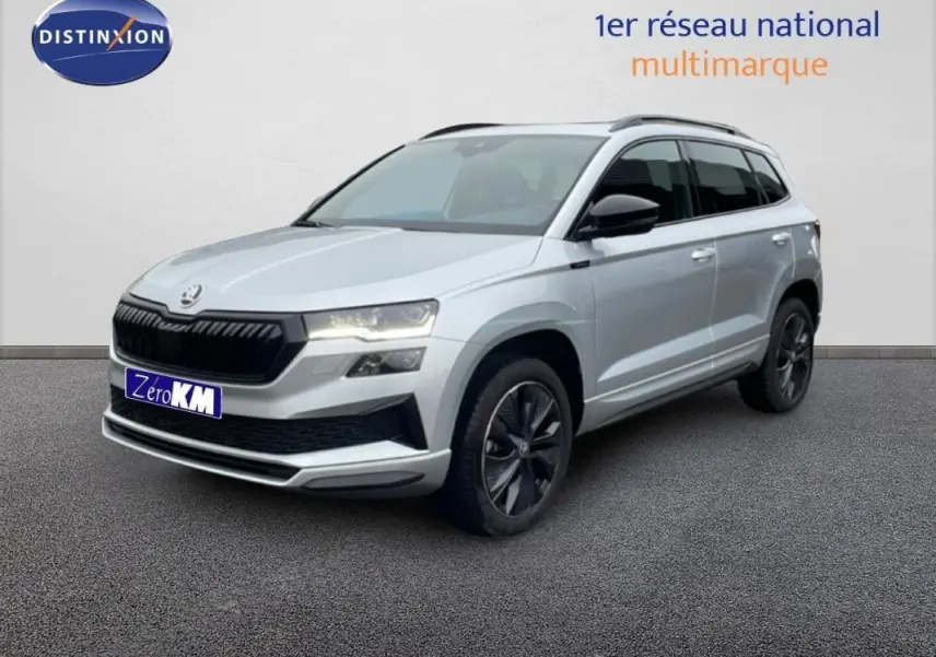 Vue 3/4 avant d'un Skoda Karoq argent 2025 avec barres de toit et jantes noires sur fond neutre.