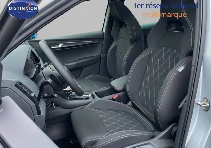 Vue intérieure côté conducteur du Skoda Karoq argent 2025, sièges sport noirs avec surpiqûres blanches et volant cuir multifonctions.