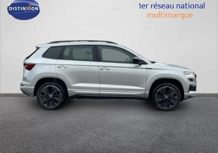 Vue de profil côté gauche d'un Skoda Karoq argent 2025 avec barres de toit et jantes noires sportline.