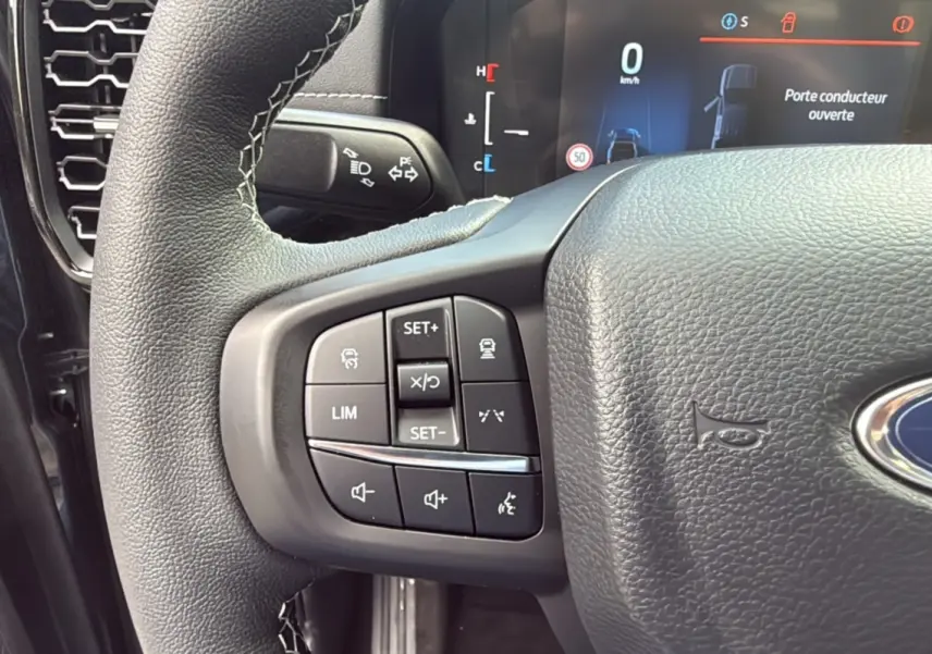 Gros plan sur le volant cuir multifonctions noir du Ford Ranger 2.3 PHEV avec commandes de régulateur et audio, tableau de bord digital visible.