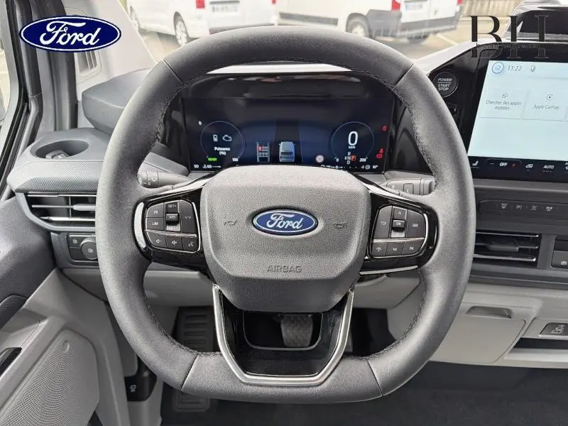 Vue rapprochée du volant multifonctions noir du Ford Transit Custom Fourgon 2026 avec tableau de bord digital et écran tactile.